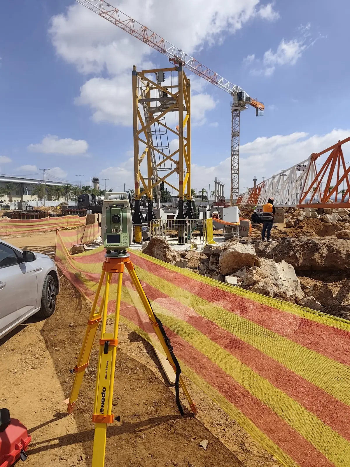 תחנה כוללת על חצובה מול ארבע רגלי השתילה של עגורן הצריח בנתב"ג, ומגדל הפיקוח של שדה התעופה ברקע