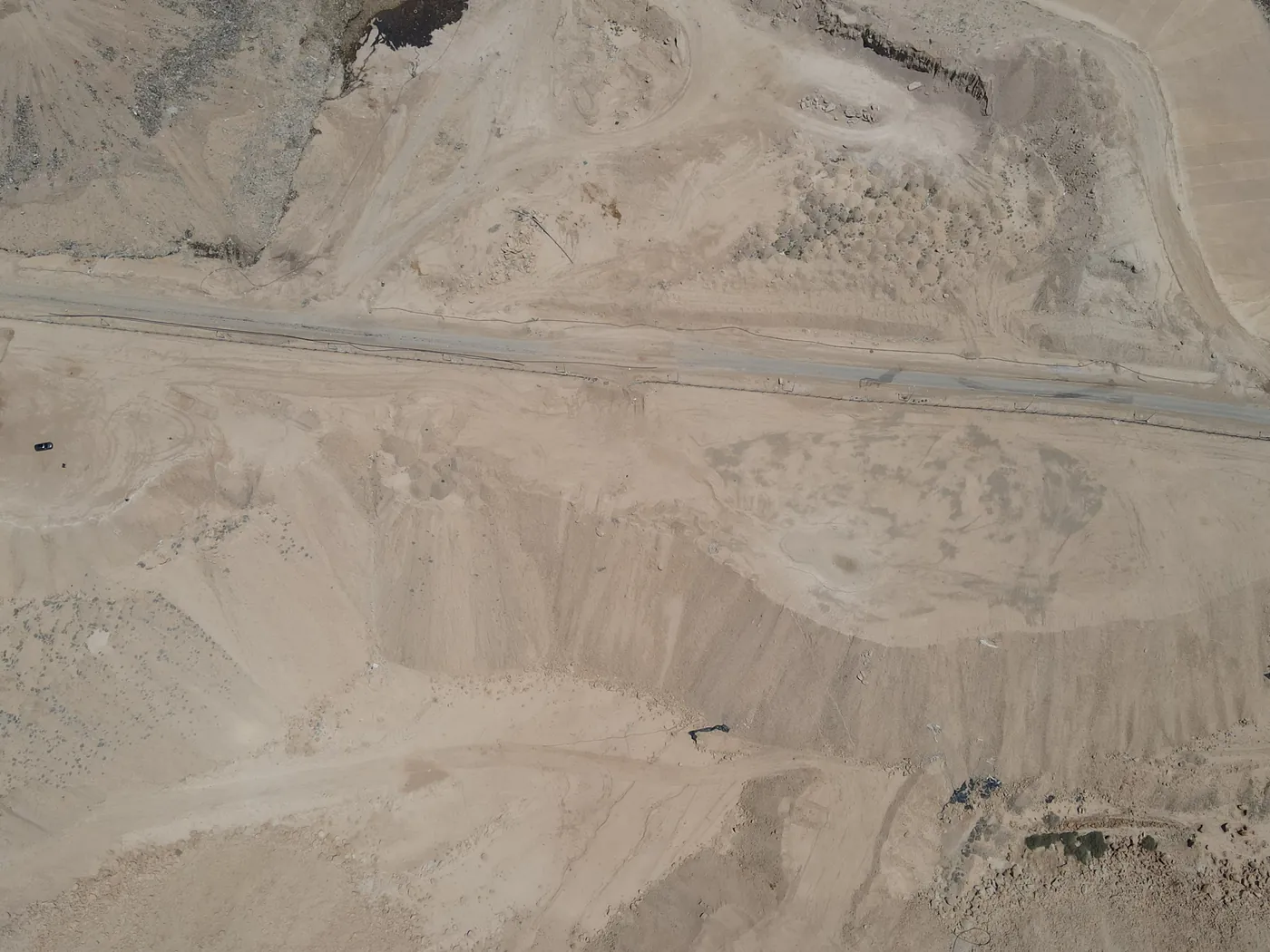 מבט רחפן על שטח התא לפני תחילת העבודות: תלוליות עפר, מדרון תלול ודרך האתר החוצה את השטח
