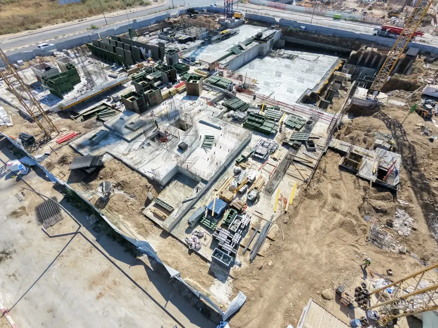 המתחם במבט אלכסוני: גרעיני מדרגות בבנייה, משטחי בטון יצוקים וטפסות על שטח המרתף המשותף