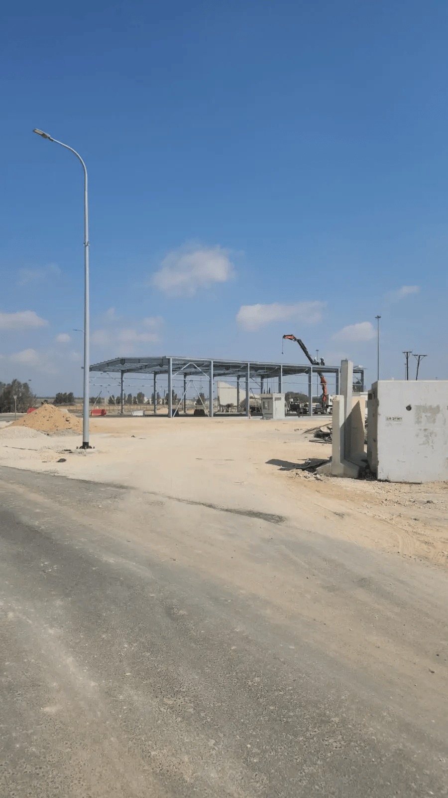 שלד פלדה של מבנה מסוף חדש בשלבי הקמה, עם מנוף משאית ומשטח עפר מיושר לפניו