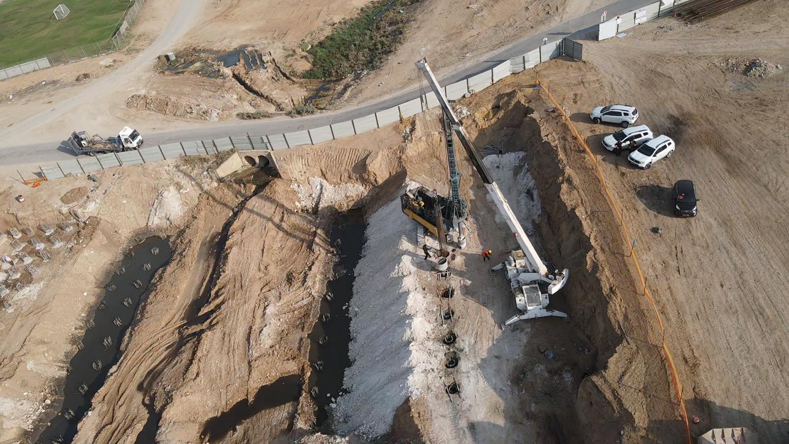 צילום אוויר של עבודות חפירה וכלונסאות בתוואי הנחל, עם מקדח כלונסאות ומנוף בתחתית החפירה