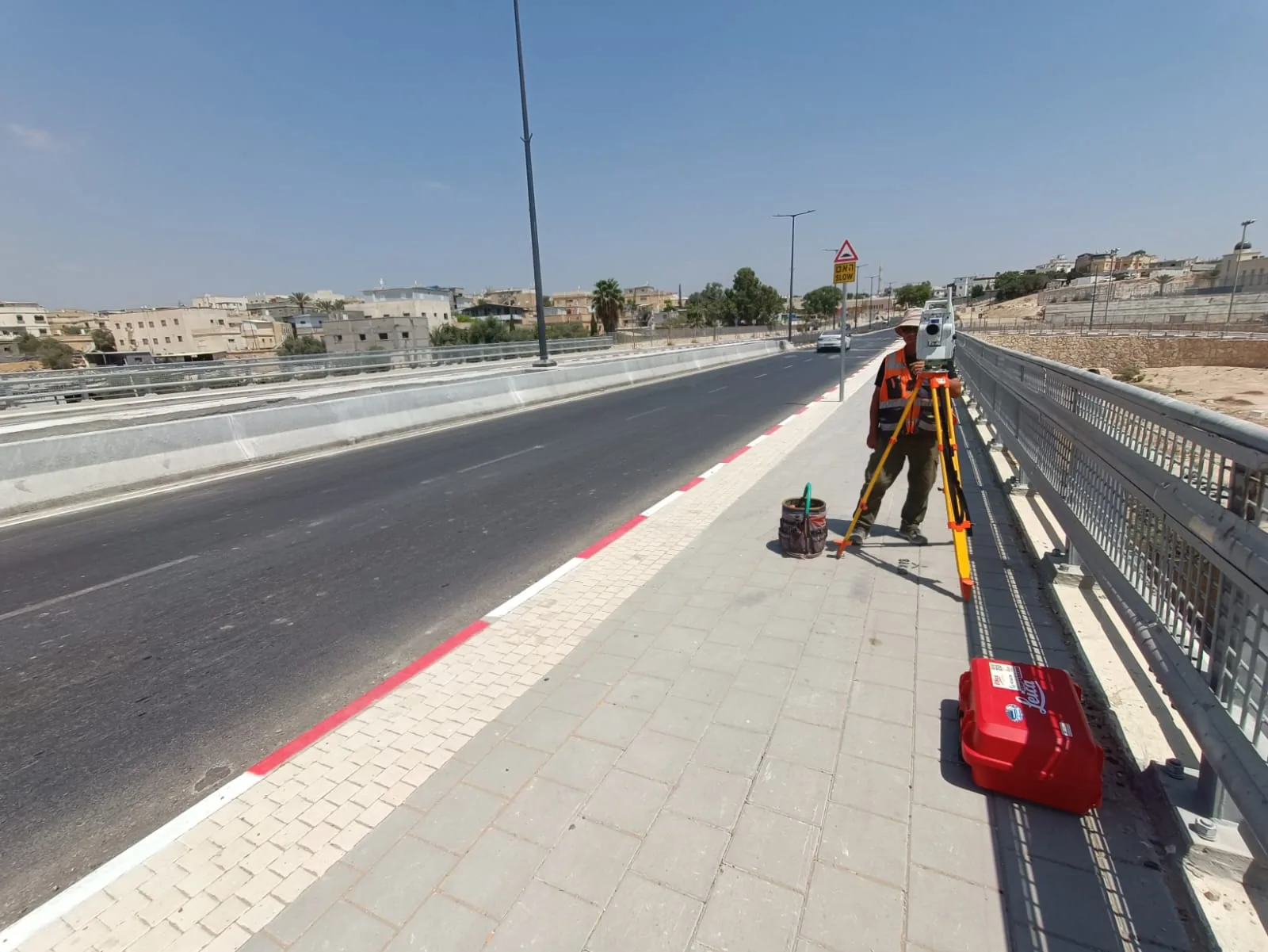 מודד מהצוות שלנו עומד על מדרכת הגשר עם תחנה כוללת לייקה על חצובה, מודד את הכביש הגמור