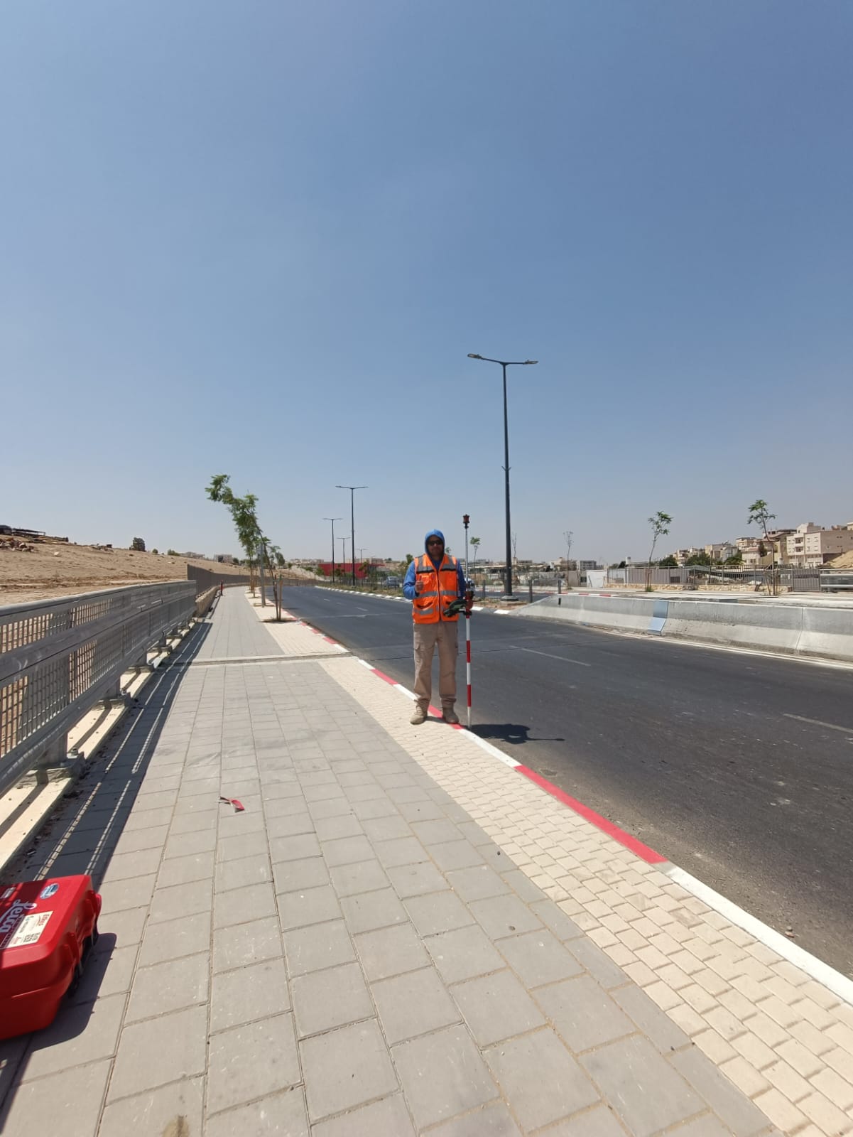 מודד מהצוות שלנו מחזיק מוט פריזמה על המדרכה החדשה, כנקודת מטרה לתחנה הטוטאלית