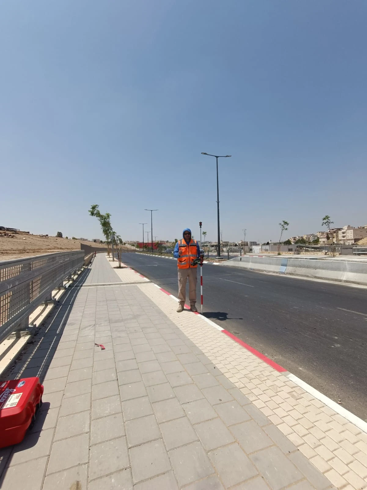 מודד מהצוות שלנו מחזיק מוט פריזמה על המדרכה החדשה, כנקודת מטרה לתחנה הכוללת