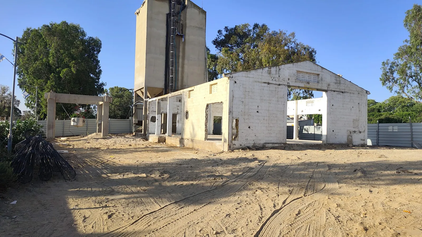 מבנה האסם הקיים לצד מגדל הסילו בקיבוץ ניר עוז, עם השטח החולי סביבו לפני תחילת העבודות