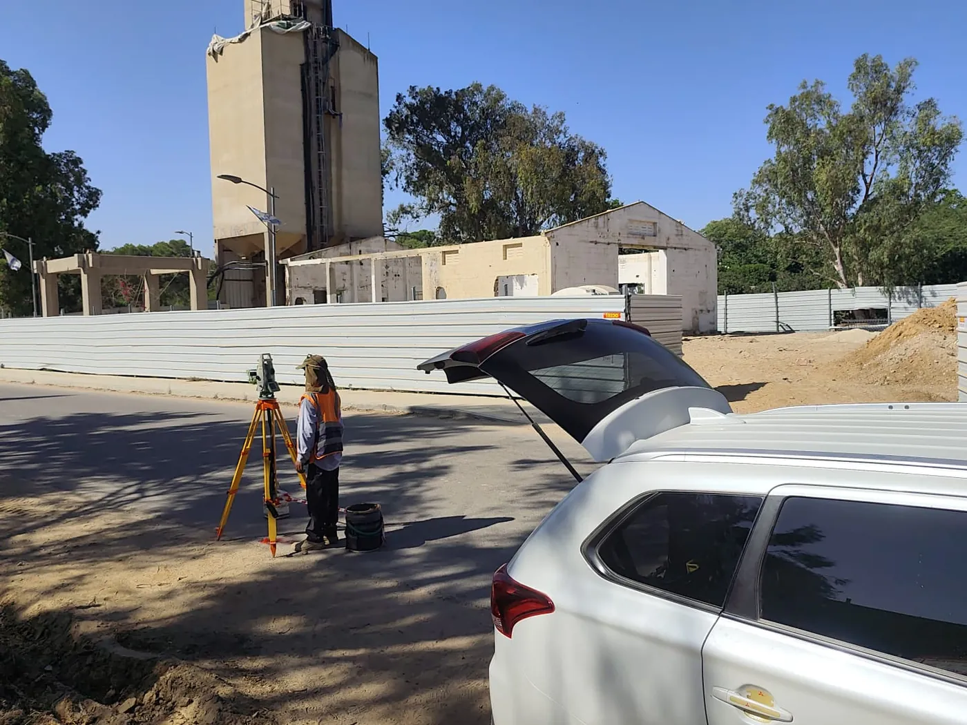 מודד מאחורי תחנה כוללת על חצובה ליד גדר האתר, ומאחוריו הסילו ומבנה האסם
