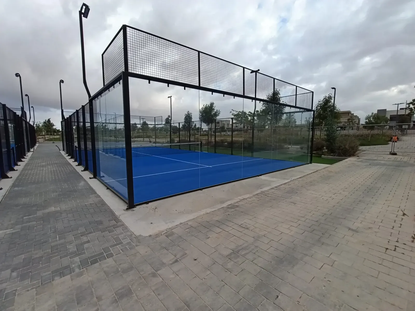מגרש פאדל שלם במבט אלכסוני, יושב על משטח בטון מוגבה עם שוליים חשופים