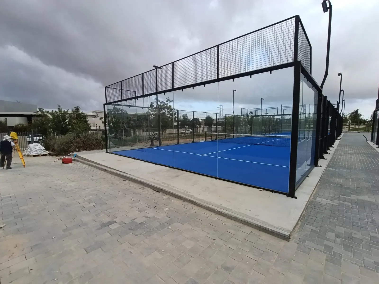 מודד מהצוות שלנו עומד עם תחנה כוללת על חצובה לצד מגרש פאדל גמור בפארק שרונית בלהבים